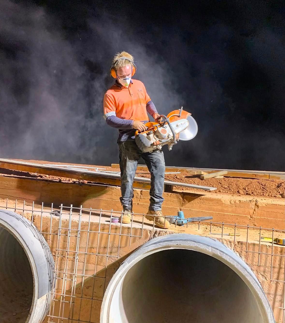 Site worker cutting steel above large concrete culvert pipes