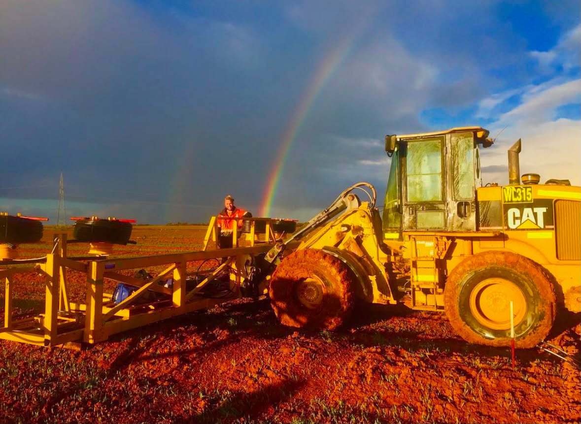 Wheel loader and site worker on an earthworks site at sunset with a rainbow overhead