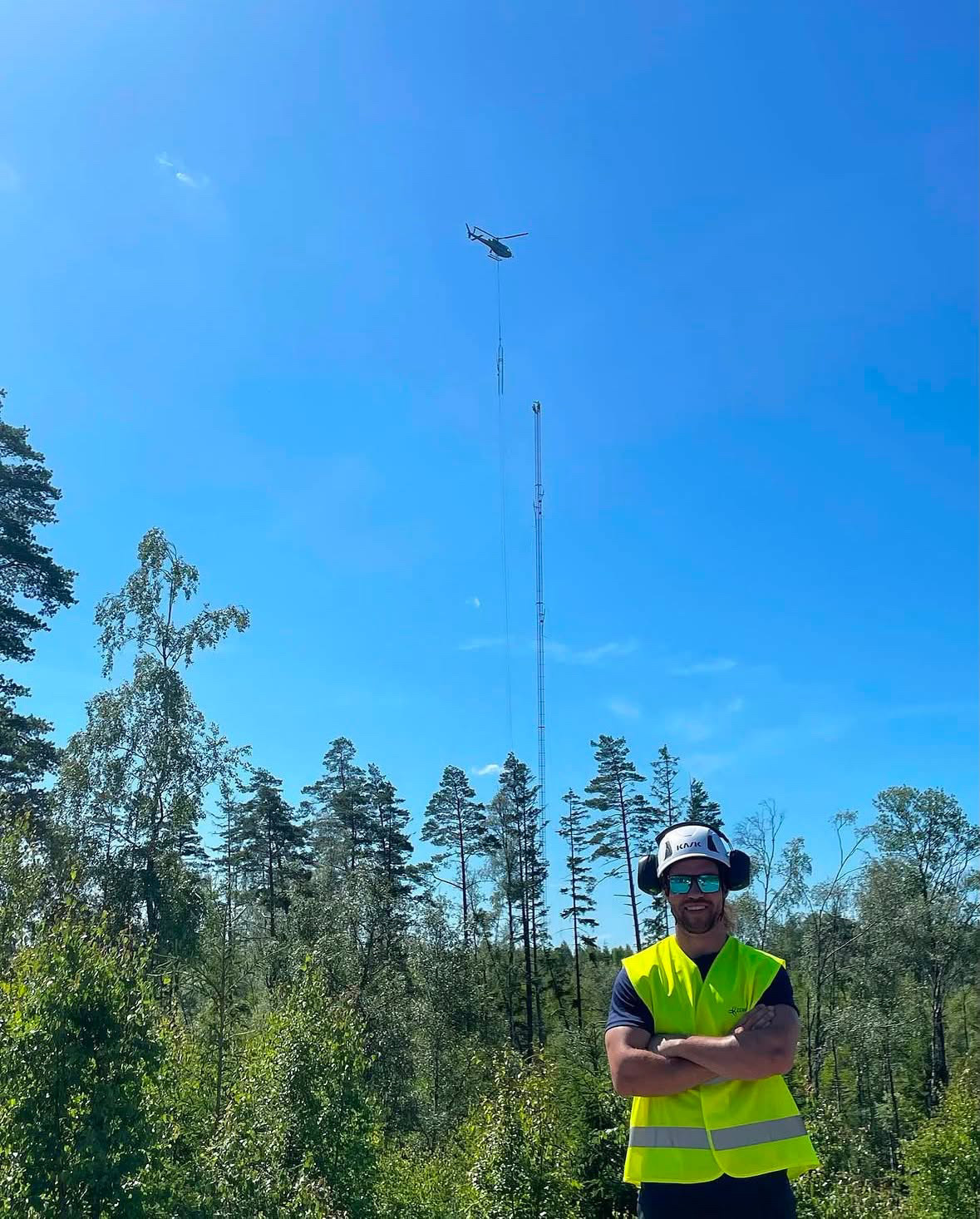 Helicopter lifting wind measurement mast sections above a forest clearing
